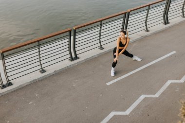 Sabahın sessizliğinde, atletik giyinen genç bir kadın şehir yolunda geriniyor, kulaklıkları takılı, vücuduna egzersiz için enerji vermeye ya da koşmaya odaklanıyor..