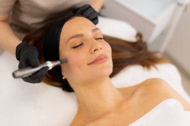 A skilled practitioner performs microneedling on a relaxed client, enhancing skin texture and rejuvenation. The tranquil spa ambiance promotes a sense of calm and well-being. clipart