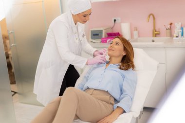 Yetenekli bir profesyonel yönetici rahatlatıcı bir klinik ortamında rahatlamış bir müşteriye kozmetik bir tedavi uygular. Atmosfer sakin, gençleşme ve kendine bakımı teşvik ediyor..