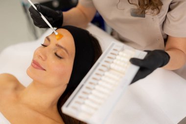 Yetenekli bir estetikçi, müşterinin alnına canlı bir retinol serumu uygular. Cilt rutinini sakinleştirici dekorla dolu sakin bir spa ortamında geliştirir..