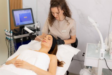 Yetenekli bir terapist müşterisinin yüzünde yüksek frekanslı terapi uygular. Huzurlu bir spa ortamında deri sağlığını ve rahatlamayı teşvik eder. Atmosfer konfor ve bakım yayar..