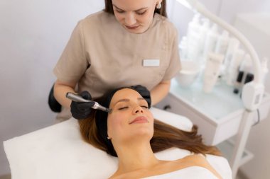 Yetenekli bir profesyonel, dingin bir klinikte, cilt gençleştirme ve güzelliği geliştirme üzerine odaklanan bir hastada mikro terapi cihazı kullanır. Çevre sakin ve steril..