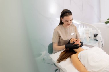 Yetenekli bir profesyonel, sakin bir kaplıcada sakin bir müşteriye rahatlatıcı bir yüz ifadesi sergiler. Huzurlu bir deneyim için cilt gençleşmesini ve nihai rahatlığı sağlar..