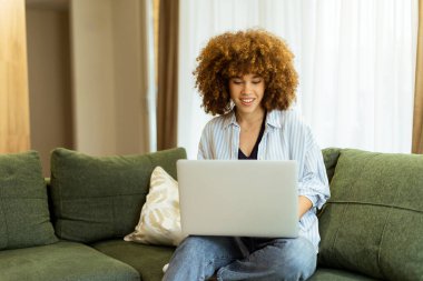 Pofuduk yeşil bir kanepede rahat bir şekilde oturan genç bir kadın dizüstü bilgisayarıyla yazı yazıyor. Büyük pencerelerden süzülen sıcak güneş ışığının tadını çıkarıyor. Odaklanma ve sükunet yayıyor..