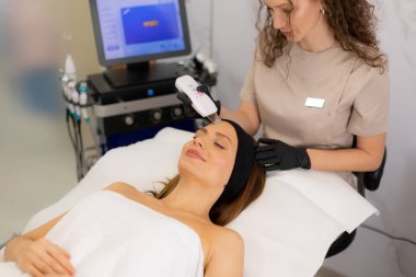 Becerikli bir terapist müşterinin alnına ultrasonik yüz masajı yapar. Rahatlama ve cilt bakımını iyileştirir..