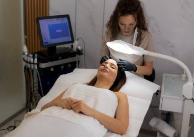 Kendini adamış bir teknisyen sakin bir müşteriye gençleştirici bir yüz tedavisi uygular, rahatlatıcı bir ortamda rahatlatıcı rahatlama ve profesyonel spa teknikleri gösterir..