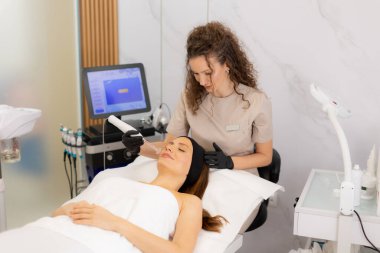 Yetenekli bir terapist müşterisinin yüzünde yüksek frekanslı terapi uygular. Huzurlu bir spa ortamında deri sağlığını ve rahatlamayı teşvik eder. Atmosfer konfor ve bakım yayar..