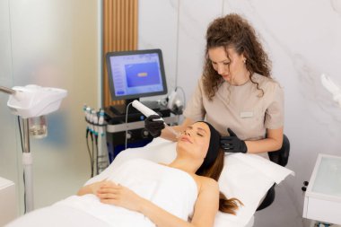 Yetenekli bir terapist müşterisinin yüzünde yüksek frekanslı terapi uygular. Huzurlu bir spa ortamında deri sağlığını ve rahatlamayı teşvik eder. Atmosfer konfor ve bakım yayar..