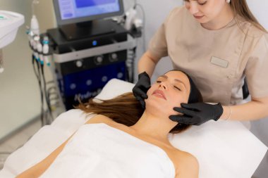 Huzurlu bir spa ortamında huzurlu bir yüz tedavisinden hoşlanan bir kadın, sakinleştirici renkler ve canlandırıcı bir deneyim sunan nazik ellerle çevrilidir..