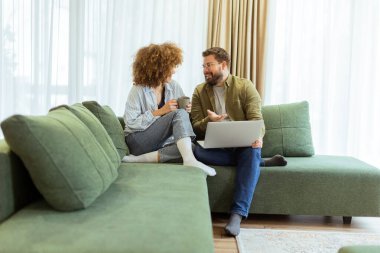 Neşeli bir çift, rahat, yeşil bir koltukta yan yana oturur. Sıcak güneş ışığı altında dizüstü bilgisayardaki fikirleri incelerken heyecan verici bir sohbete dalarlar.