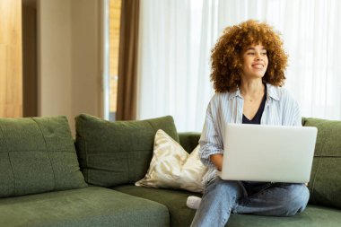Pofuduk yeşil bir kanepede rahat bir şekilde oturan genç bir kadın dizüstü bilgisayarıyla yazı yazıyor. Büyük pencerelerden süzülen sıcak güneş ışığının tadını çıkarıyor. Odaklanma ve sükunet yayıyor..