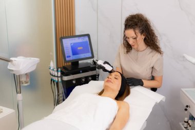 Huzurlu bir ayar müşterinin cildinde ultrasonik yüz masajı yapan yetenekli bir pratisyen gösteriyor. Parlak bir cilt için derin temizlik ve gevşemeyi teşvik ediyor..