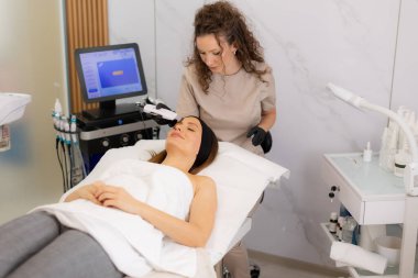 Huzurlu bir ayar müşterinin cildinde ultrasonik yüz masajı yapan yetenekli bir pratisyen gösteriyor. Parlak bir cilt için derin temizlik ve gevşemeyi teşvik ediyor..