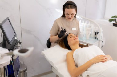 Yetenekli bir profesyonel, dingin bir klinikte, cilt gençleştirme ve güzelliği geliştirme üzerine odaklanan bir hastada mikro terapi cihazı kullanır. Çevre sakin ve steril..