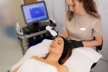 Becerikli bir terapist müşterinin alnına ultrasonik yüz masajı yapar. Rahatlama ve cilt bakımını iyileştirir..