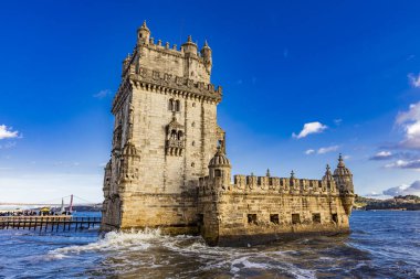 Belem Kulesi, Tagus Nehri 'nin kıyısından gururla yükselir. Parlak mavi gökyüzünün altındaki karmaşık mimarisini gözler önüne serer..