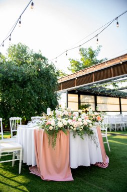 Canlı çiçekli süsler zarif bir şekilde yuvarlak bir masayı beyaz sandalyelerle süslüyor, yemyeşil çimlere kuruluyor, şenlikli bir toplantı için büyüleyici bir atmosfer yaratıyor..