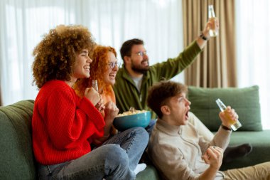 Dostlar sıcak bir oturma odasında toplanırken, kahkaha ve heyecan havayı dolduruyor, içkilerin tadını çıkarıyor ve keyifli bir maç sırasında en sevdikleri spor takımını kutluyorlar..
