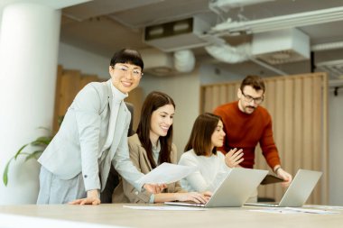 Çeşitli profesyonellerden oluşan bir grup dinamik bir beyin fırtınası yapıyor. Fikir alışverişinde bulunurlar, dizüstü bilgisayarlarda işbirliği yaparlar ve belgeleri açık ve parlak bir çalışma alanında paylaşırlar..