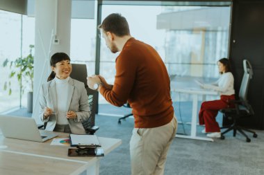 İki profesyonel, şık bir ofis çalışma alanında dizüstü bilgisayardaki bilgileri incelerken canlı bir tartışmaya girişiyor. Coşkuları takım çalışması ve yenilikleri vurguluyor.