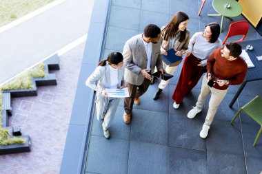 Beş profesyonelden oluşan bir grup dışarıda bir terasta toplanarak fikir ve planlarını paylaşıyor. Parlak bir atmosfer içinde işbirlikçi bir ruh sergileyen çeşitli cihazlar ve kağıtlar tutuyorlar..