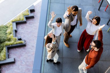 Beş bireyden oluşan canlı bir toplantı, yoldaşlık ve takım çalışmasını kutluyor, açık gökyüzü altında, yeşilliklerle dolu modern bir açık alanda birbirlerinin arkadaşlığının tadını çıkarıyorlar..