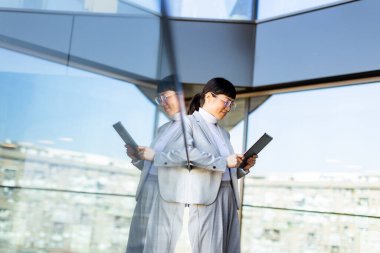 Kendine güvenen bir girişimci elinde tabletle parlak, çağdaş bir ofiste duruyor. Büyüleyici şehir silüeti büyük cam pencerelerden görülebilir..