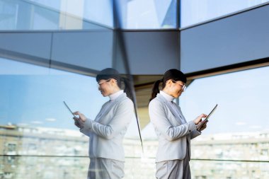 Kendine güvenen bir girişimci elinde tabletle parlak, çağdaş bir ofiste duruyor. Büyüleyici şehir silüeti büyük cam pencerelerden görülebilir..