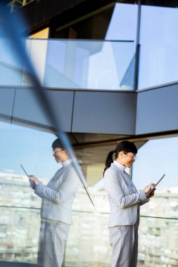 Kendine güvenen bir girişimci elinde tabletle parlak, çağdaş bir ofiste duruyor. Büyüleyici şehir silüeti büyük cam pencerelerden görülebilir..