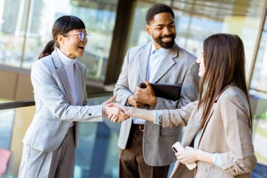 Şık iş kıyafeti giyen üç profesyonel, parlak, çağdaş ofis ortamında şehir görüşleriyle fikirleri tartışırken dostça bir tokalaşma paylaşıyorlar..