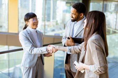 Şık iş kıyafeti giyen üç profesyonel, parlak, çağdaş ofis ortamında şehir görüşleriyle fikirleri tartışırken dostça bir tokalaşma paylaşıyorlar..