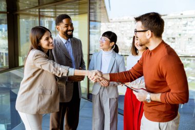 Bir grup profesyonel çağdaş bir ofiste fikirleri tartışırken dostça tokalaşıyor. Sıcak atmosfer, çeşitli katılımcılar arasında bağlantı ve takım çalışmasını teşvik ediyor.