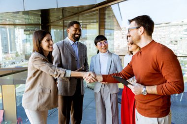 Bir grup profesyonel çağdaş bir ofiste fikirleri tartışırken dostça tokalaşıyor. Sıcak atmosfer, çeşitli katılımcılar arasında bağlantı ve takım çalışmasını teşvik ediyor.
