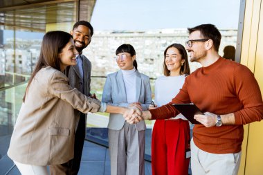 Parlak bir ofiste profesyonellerin canlı bir araya gelmesi, el sıkışmaları, gülümsemeleri ve yenilikçi stratejileri tartışmaları, ekip üyeleri arasında işbirliğini ve bağlantıyı teşvik etmeleri,.