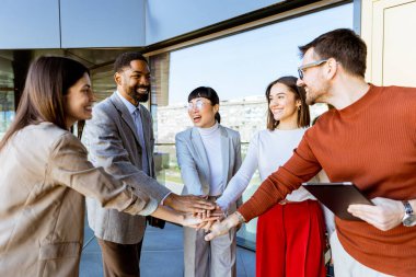 Çağdaş bir ofis alanında toplanan beş profesyonelden oluşan bir grup, yaklaşan projeleri için fikir alışverişinde bulunurken gülümseyip el ele tutuşuyor..