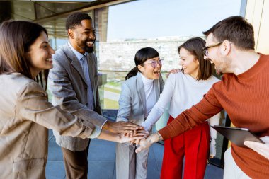 Çağdaş bir ofis alanında toplanan beş profesyonelden oluşan bir grup, yaklaşan projeleri için fikir alışverişinde bulunurken gülümseyip el ele tutuşuyor..