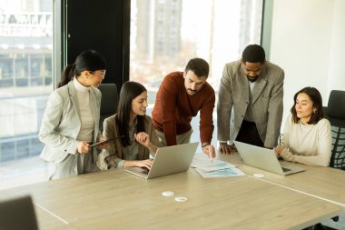 Çeşitli profesyonellerden oluşan bir grup, bir konferans masası etrafında dinamik bir beyin fırtınası yapıyor, fikirlerini paylaşıyor ve parlak bir ofis alanında dizüstü bilgisayar ve notlarla etkileşime giriyor..