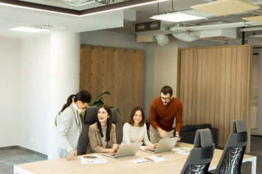 Dört profesyonel, doğal ışıkla dolu modern bir ofis ortamında dizüstü bilgisayarların etrafında dinamik bir tartışmaya girişiyor. Bir projede işbirliği yaparken fikir akışı.