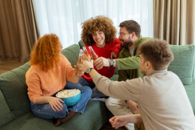 Dört arkadaş yeşil bir kanepede rahatça oturup içkilerini kadeh kaldırıyorlar. Kahkaha, sıcak bir atmosferle çevrili bir neşe anını paylaştıkça havayı doldurur..