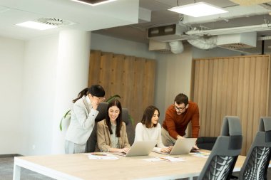 Dört profesyonel, doğal ışıkla dolu modern bir ofis ortamında dizüstü bilgisayarların etrafında dinamik bir tartışmaya girişiyor. Bir projede işbirliği yaparken fikir akışı.