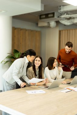 Dört profesyonel, doğal ışıkla dolu modern bir ofis ortamında dizüstü bilgisayarların etrafında dinamik bir tartışmaya girişiyor. Bir projede işbirliği yaparken fikir akışı.