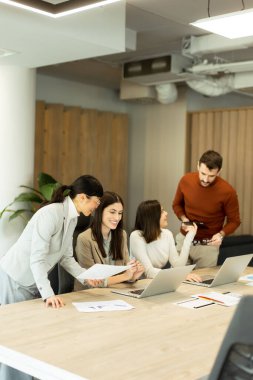 Dört profesyonel, doğal ışıkla dolu modern bir ofis ortamında dizüstü bilgisayarların etrafında dinamik bir tartışmaya girişiyor. Bir projede işbirliği yaparken fikir akışı.