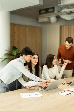 Dört profesyonel, doğal ışıkla dolu modern bir ofis ortamında dizüstü bilgisayarların etrafında dinamik bir tartışmaya girişiyor. Bir projede işbirliği yaparken fikir akışı.