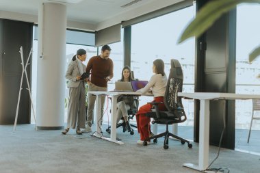 Dört profesyonel, doğal ışıkla dolu modern bir ofis ortamında dizüstü bilgisayarların etrafında dinamik bir tartışmaya girişiyor. Bir projede işbirliği yaparken fikir akışı.