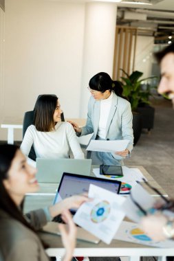 Çağdaş bir çalışma alanında, bir ekip canlı bir tartışma içine girer, büyük bir masa etrafında fikirler ve belgeler paylaşır. İfadeleri coşku ve takım çalışmasını yansıtıyor.