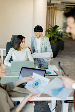 Çağdaş bir çalışma alanında, bir ekip canlı bir tartışma içine girer, büyük bir masa etrafında fikirler ve belgeler paylaşır. İfadeleri coşku ve takım çalışmasını yansıtıyor.