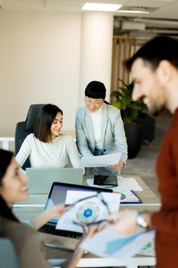 Çağdaş bir çalışma alanında, bir ekip canlı bir tartışma içine girer, büyük bir masa etrafında fikirler ve belgeler paylaşır. İfadeleri coşku ve takım çalışmasını yansıtıyor.