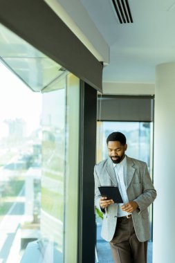 İyi giyimli bir adam, çağdaş bir ofiste geniş bir pencereden bakarken fikirlerini yansıtır. Güneş ışığı mekanı aydınlatır, ilham için sakin bir atmosfer yaratır..