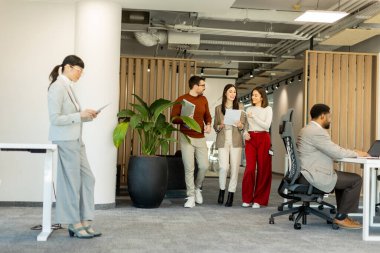 Bir grup profesyonel, dokümanları incelerken, yeşil ve çağdaş çalışma alanlarında takım çalışması ve yaratıcılığı somutlaştırırken, canlı tartışmalara girişiyor..