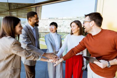 Çağdaş bir ofis alanında toplanan beş profesyonelden oluşan bir grup, yaklaşan projeleri için fikir alışverişinde bulunurken gülümseyip el ele tutuşuyor..